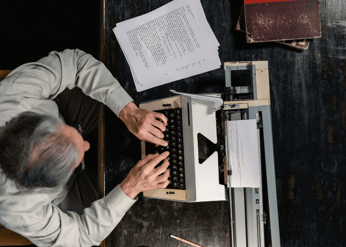 Writing a book on a typewriter with a manuscript draft viewed from above.