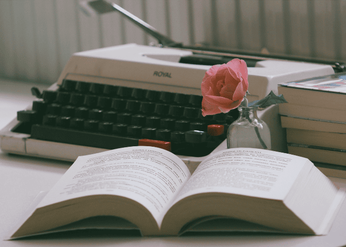 Memoir Ghostwriter inspiration with a vintage typewriter, open book, and rose on a writer's desk.